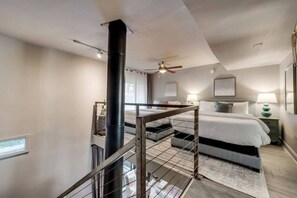 A bedroom with a large bed, a ceiling fan, a black column, and a staircase with a metal railing. - Modern 3-bed loft with pool, courtyard, and prime walkable Dallas location. (Dallas)