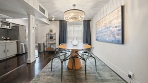 A modern kitchen with stainless steel appliances, a dining area with a round table and chairs, and a large abstract painting on the wall.