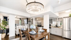 Ett rymligt kök med moderna vitvaror, en matplats med en kristallkrona och en mysig sittgrupp med en växt.