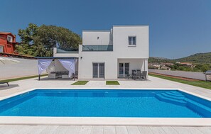 Una casa moderna de dos pisos con piscina, un espacio cubierto para sentarse al aire libre y vistas del paisaje circundante.