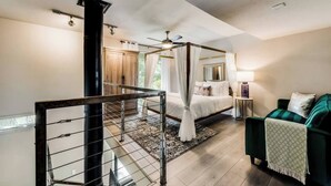 A bedroom with a four-poster bed, a ceiling fan, a nightstand, and a green armchair. - Spacious 2-story loft with king suite, fireplace, and resort-style amenities. (Dallas)