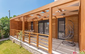 Relax on the covered patio with a seating area, table, and chairs, surrounded by lush greenery and a stone wall.