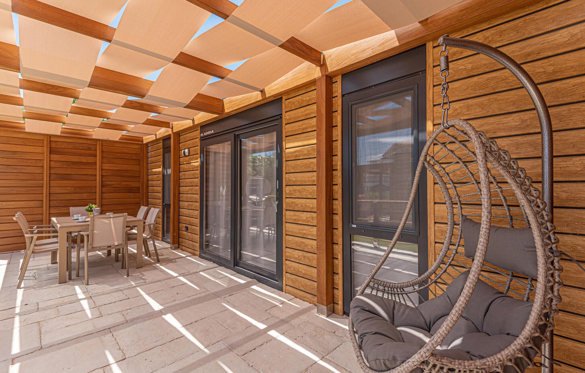 A wooden deck with a hanging chair, a table with chairs, and large windows.