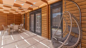 A wooden deck with a hanging chair, a table with chairs, and large windows.