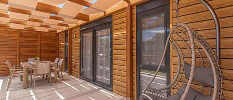 A wooden deck with a hanging chair, a table with chairs, and large windows.