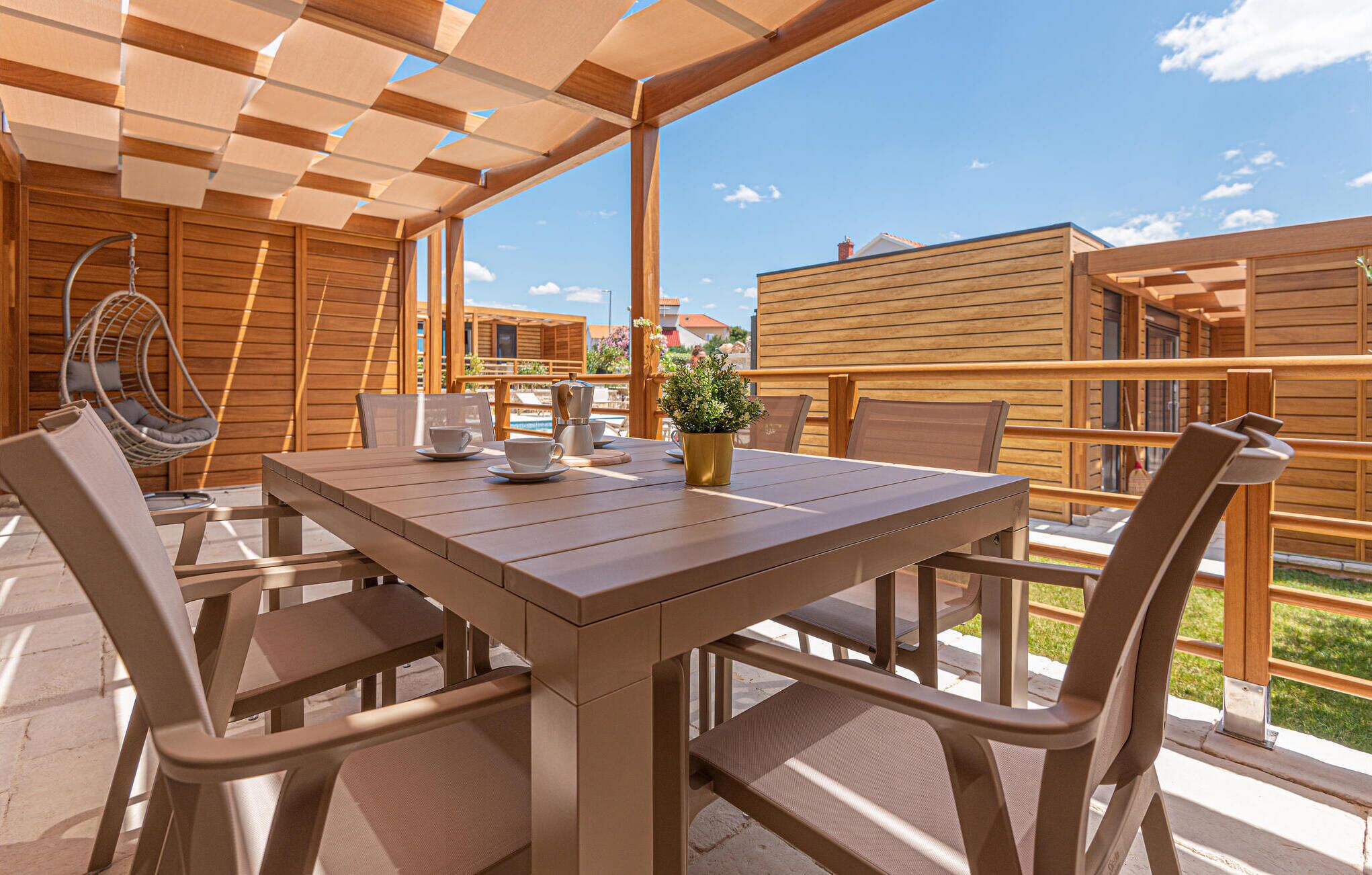 A wooden deck with a table and chairs, a hanging chair, and a potted plant.