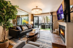 A modern living room with a fireplace, leather sofa, coffee table, and a large TV screen.