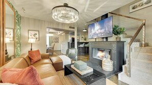 Ein modernes Wohnzimmer mit einer Ledersofa, einem Kamin, einem Fernseher und einer Chandelieber.