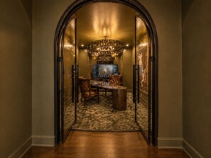 An arched doorway leading to a dining area with a chandelier, a television, and a framed artwork on the wall.