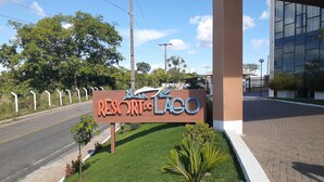 A sign for 'Resort do Lago' with a paved road and greenery in the background. - Resort do Lago - dinamicaTur (Caldas Novas)