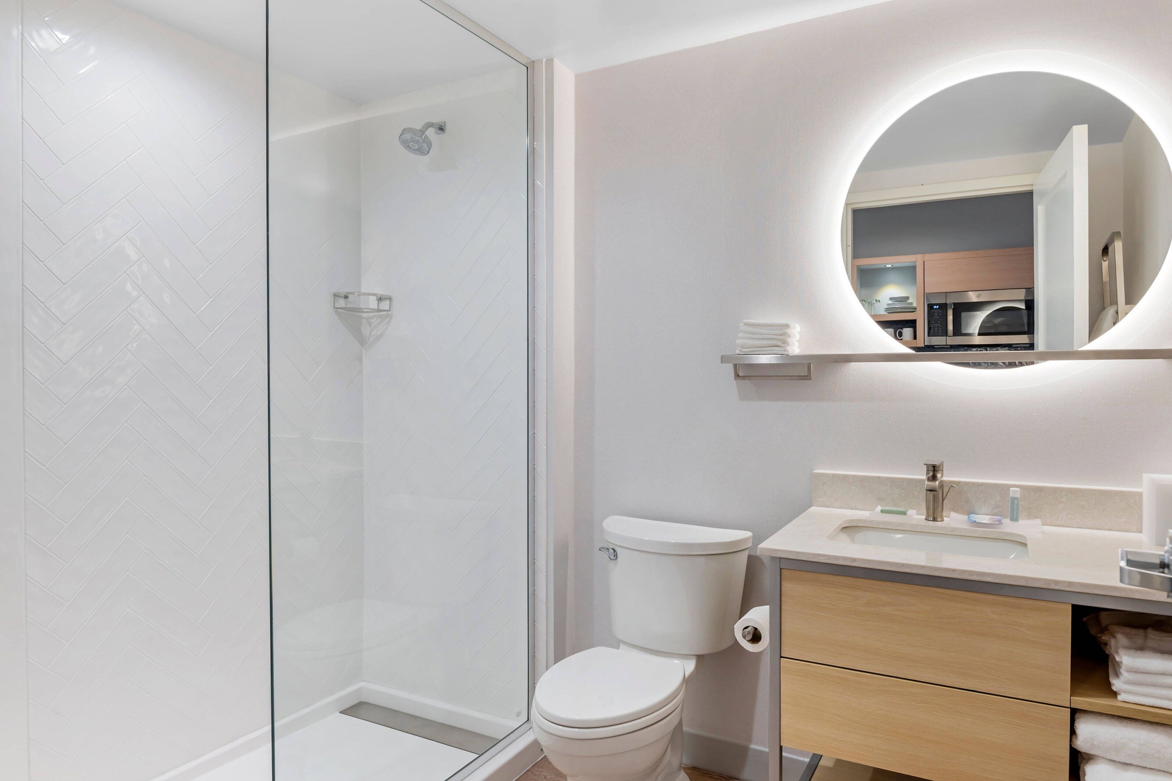A modern bathroom with a glass shower enclosure, a toilet, a sink with a mirror above it, and a towel rack.