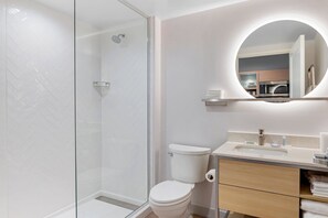 Een moderne badkamer met een douchecabine van glas, een toilet, een wastafel met spiegel erboven en een handdoekhouder.