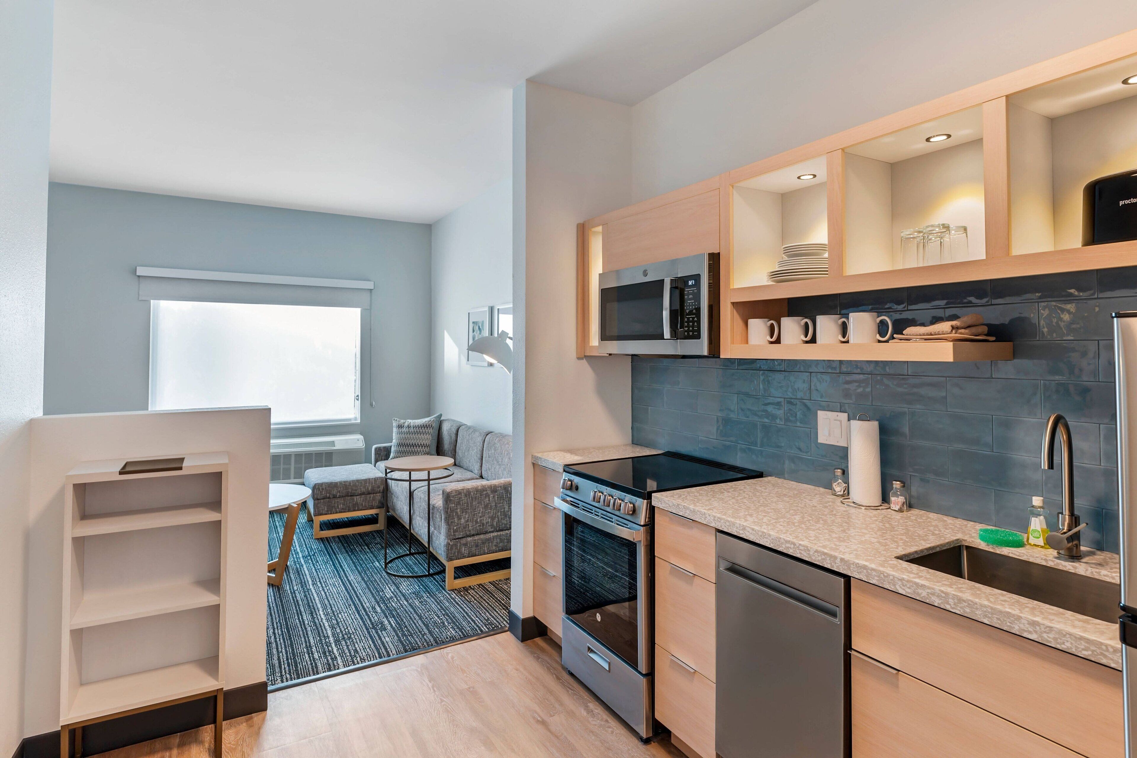 A compact kitchen with a microwave, stove, and dishwasher. There is a small seating area with a sofa and a round table.