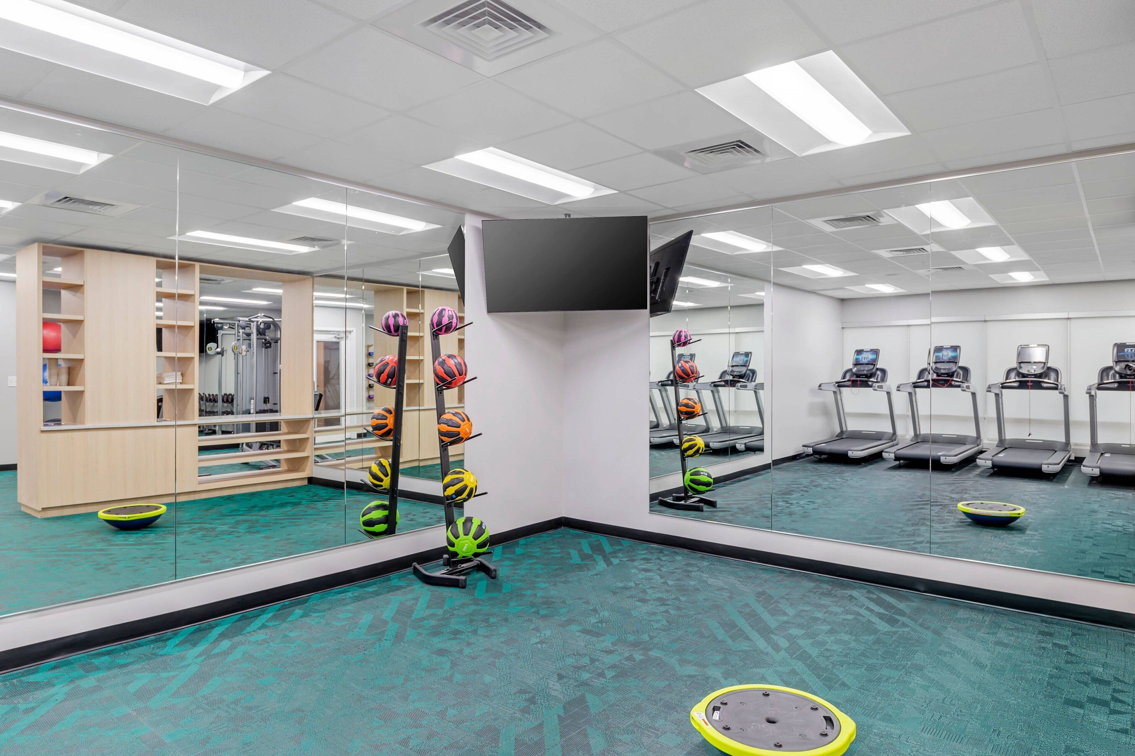 Une salle de sport équipée de matériel d’exercice, de tapis de course et dotée d’un mur recouvert de miroirs.