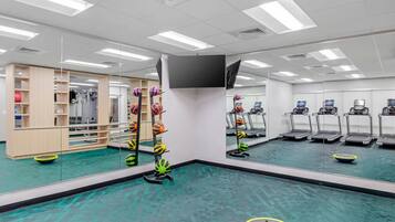 Une salle de sport équipée de matériel d’exercice, de tapis de course et dotée d’un mur recouvert de miroirs.