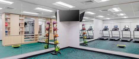 A gym with exercise equipment, treadmills, and a mirrored wall.