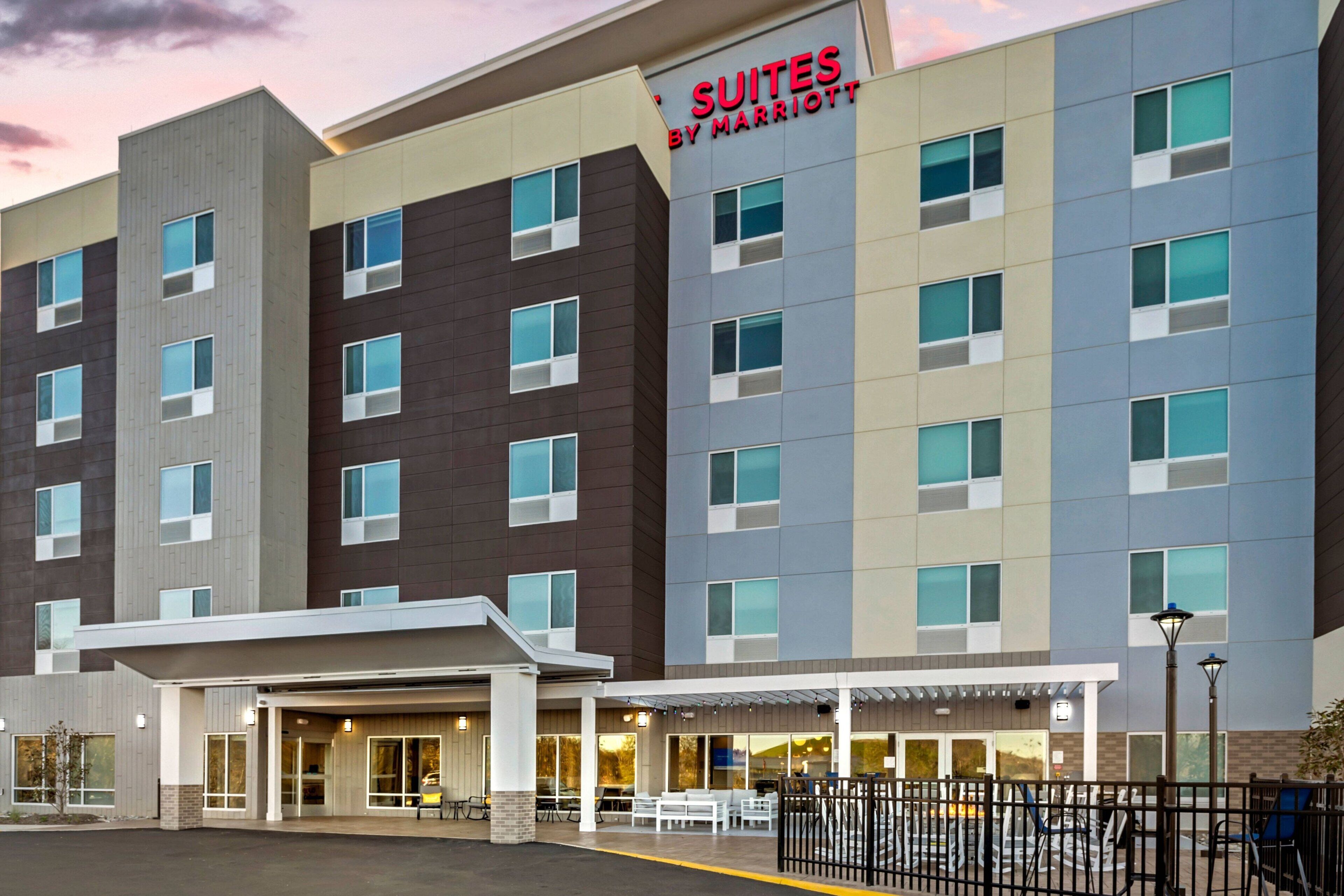 A multi-story hotel with a sign reading "Suites by Marriott" and a covered outdoor area with tables and chairs.