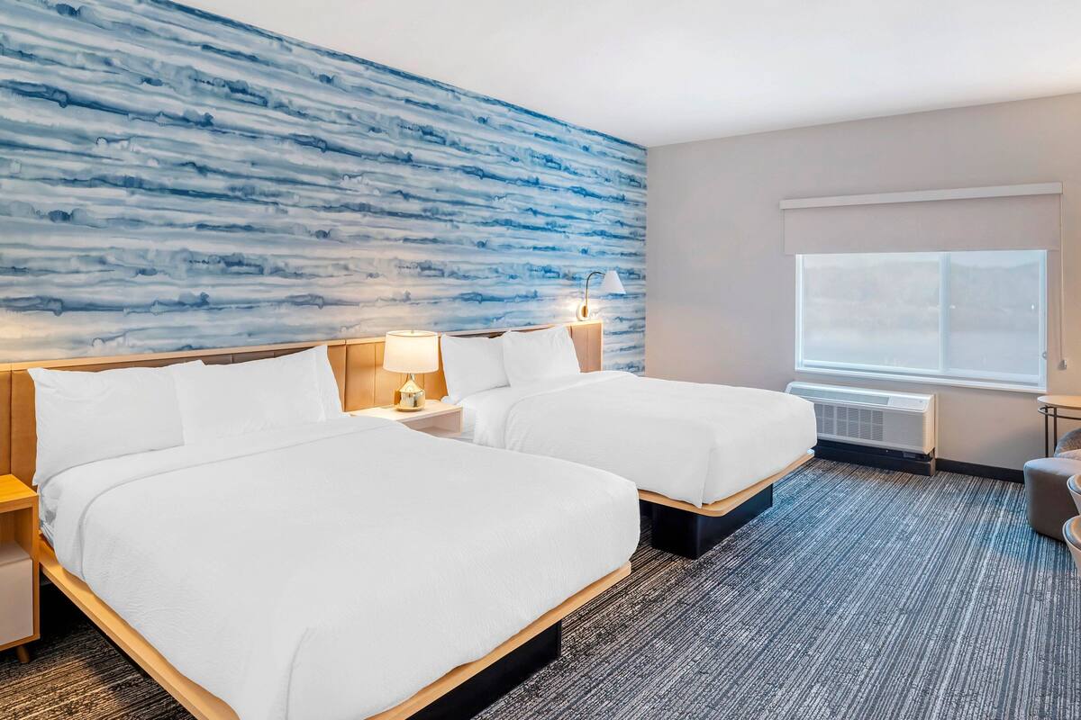 Une chambre d’hôtel avec deux lits, une grande fenêtre et un mur bleu à texture.