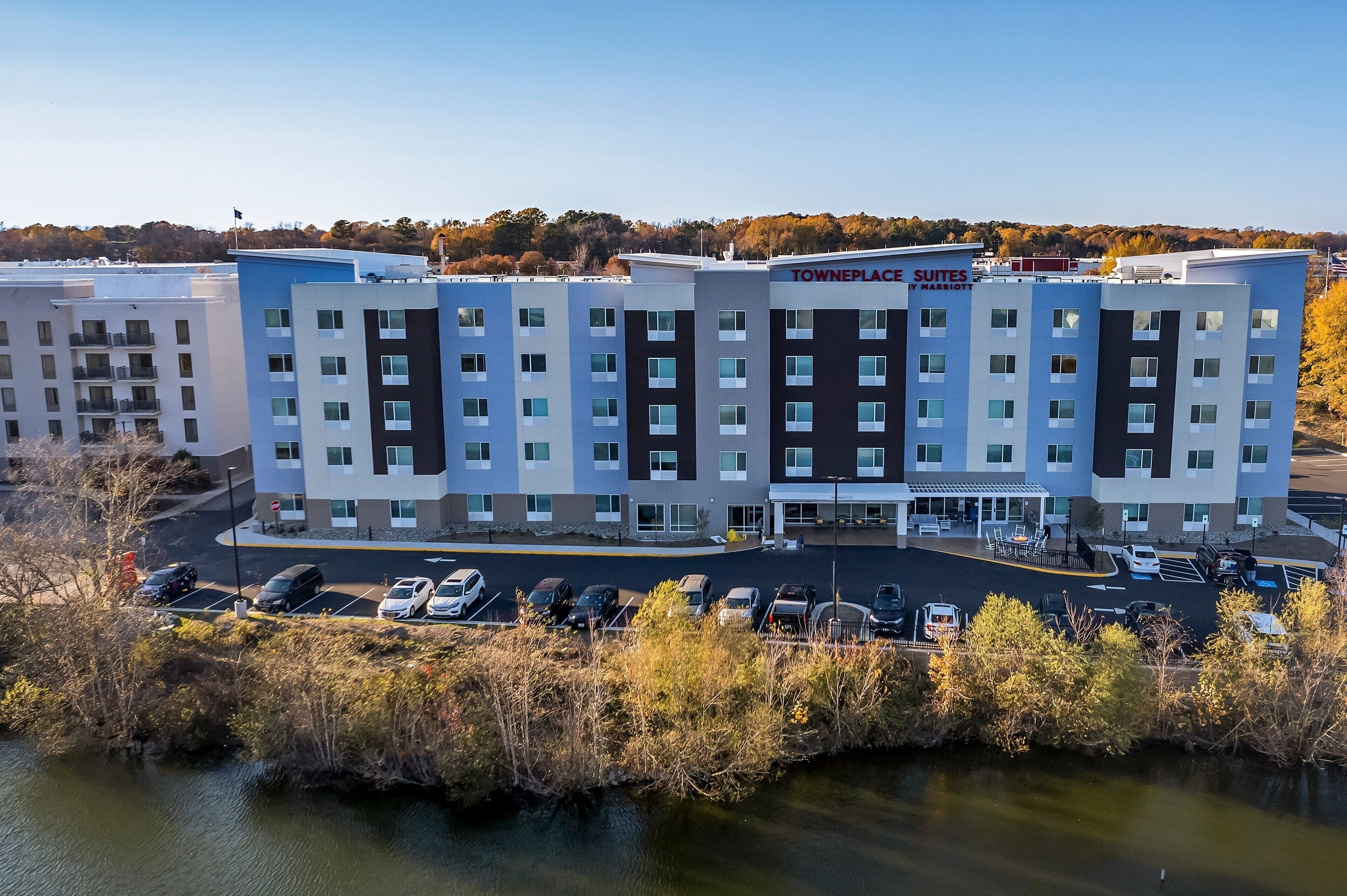 A multi-story hotel with a modern design, featuring a parking lot and a body of water in the foreground.