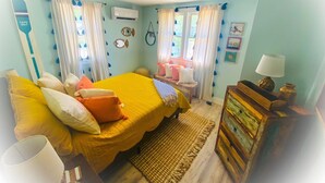 Een slaapkamer met een bed, kussens, een dressoir en een raam met gordijnen.