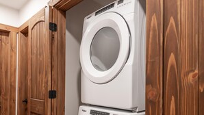 Une buanderie équipée de deux machines à laver à chargement frontal superposées et de meubles de rangement en bois.