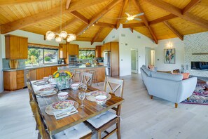 Una cocina amplia con armarios de madera, un comedor con mesa de madera dispuesta para cuatro personas, y una sala de estar con sofá y televisión.