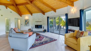 Ein geräumiges Wohnzimmer mit Kamin, zwei Sofas, einem großen Fernseher und Blick ins Freie.