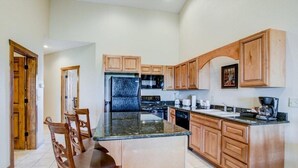 A kitchen with wooden cabinets, a granite countertop, a refrigerator, a microwave, and a coffee maker.