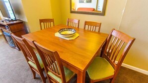 Uma área de refeições com mesa de madeira e seis cadeiras, uma tigela sobre a mesa e um quadro na parede.