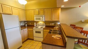 Una cocina compacta con armarios de madera, un refrigerador, un microondas, una estufa y un lavaplatos.