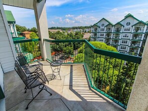 A balcony with outdoor furniture, a view of a residential area with multi-story buildings, and a clear sky.