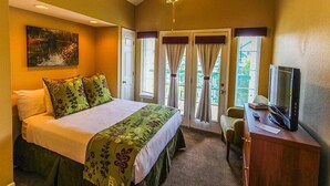 Hotelkamer met een bed, een bureau met een televisie, een plafondventilator en een raam met gordijnen.