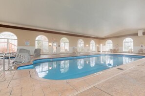 Ein Hallenbad mit klarem Wasser, gefliestem Boden und Bogenfenstern.