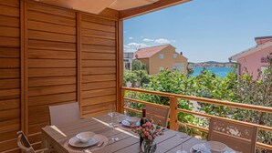 Un balcon en bois avec une table dressée pour le dîner, donnant sur une ville côtière avec ses bâtiments et un ciel bleu dégagé.