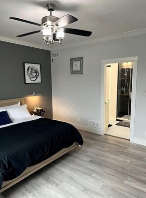 Une chambre à coucher comprenant un lit, un ventilateur de plafond, une horloge et un espace douche.