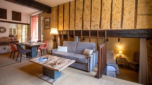 Een gezellige woonkamer met een stenen muur, een houten balk, een bank, een salontafel en een eethoek met stoelen en een tafel.