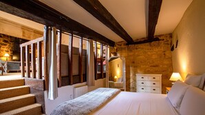 Een slaapkamer met een groot bed, een houten trap, een stenen muur en een witte ladekast.