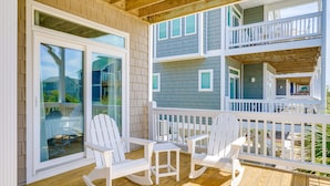 Um deck de madeira com cadeiras de balanço brancas e uma mesa, com vista para uma área residencial.