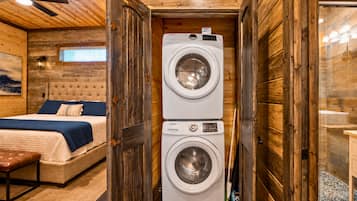 A compact room with a bed, a washing machine, and a bench.