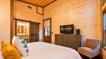 A wooden cabin bedroom with a bed, a dresser, a chair, and a television displaying 'TreeLine Vacation Rentals'.