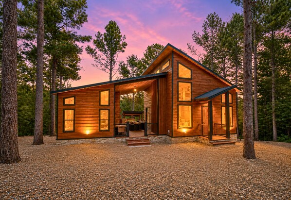 A modern log cabin with a deck, surrounded by trees.
