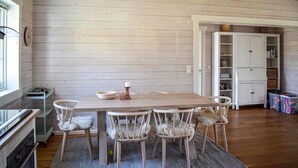 A dining area with a wooden table and chairs, a rug, and a kitchen area with cabinets and a refrigerator.