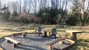 A circular outdoor seating area with benches and chairs, surrounded by gravel and trees.