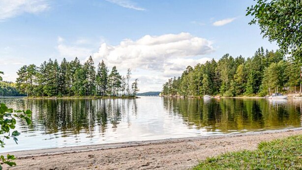 A calm lake with a sandy beach and dense forest on both sides.