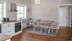 A kitchen with wooden walls, a dining table with chairs, a stove, and a hanging light fixture.