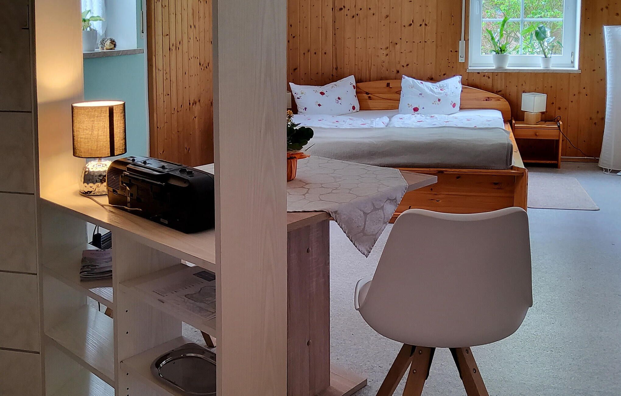 A bedroom with a bed, bedside table, lamp, and a chair.