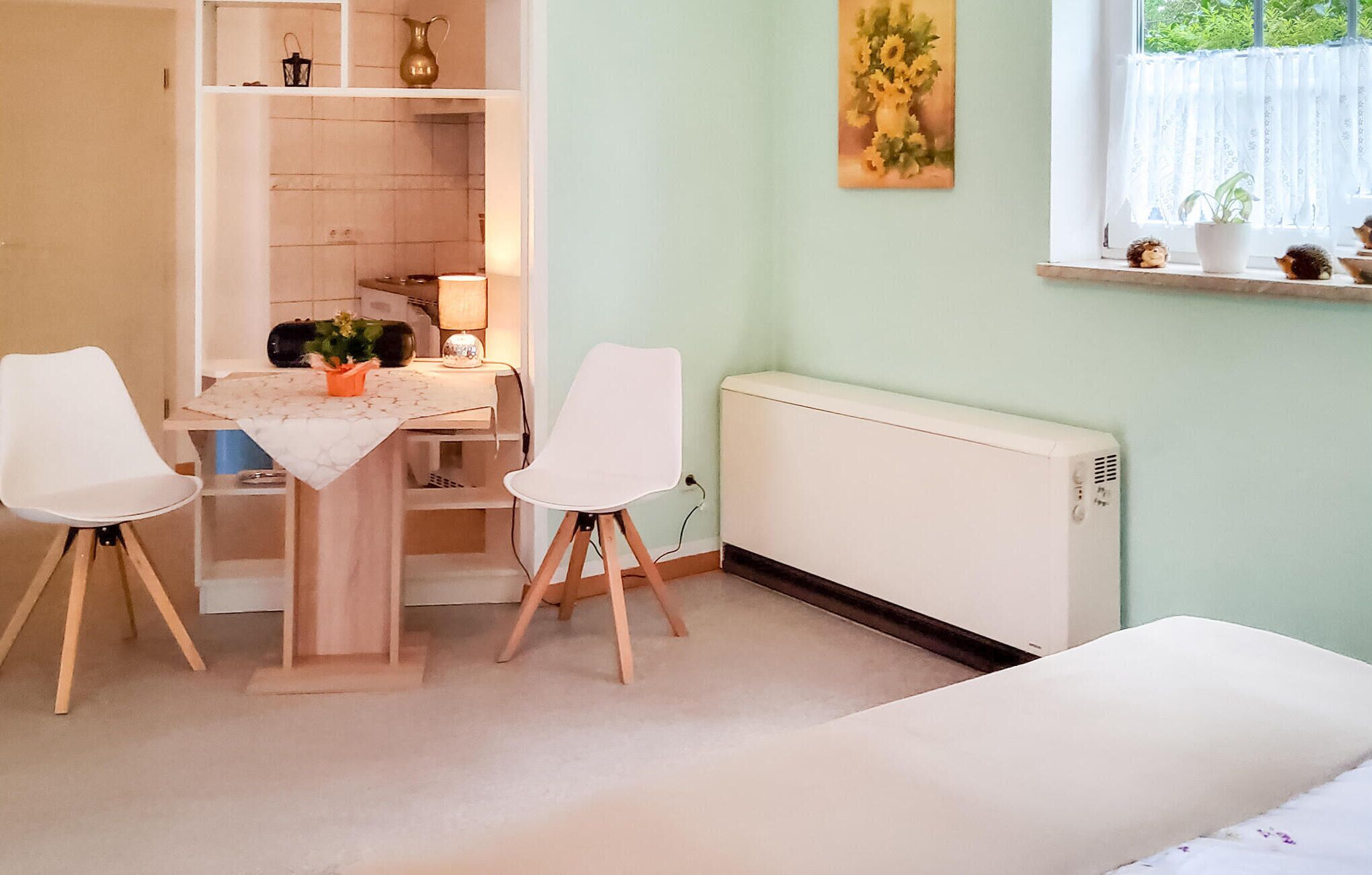 Een kamer met een tafel, twee stoelen, een radiator en een raam met een plant op de vensterbank.