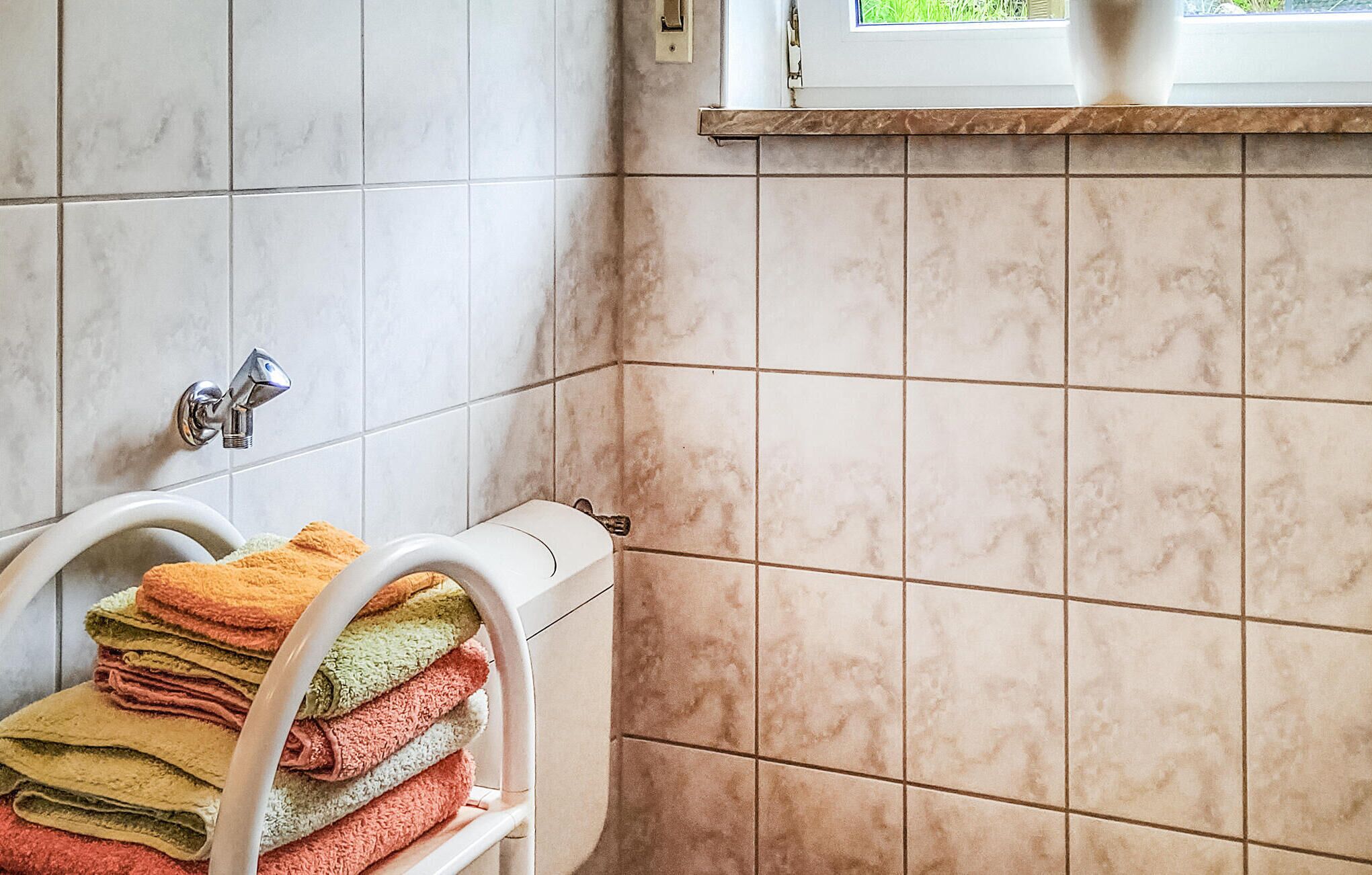 Ein Badezimmer mit weißen Marmorfliesen, einem weißen Handtuchhalter mit gefalteten Handtüchern und einem Fenster über dem Waschbecken.