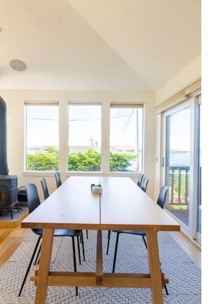 A long, rectangular dining table with chairs, large windows, and a view of greenery outside. - Ocean Views with Private Hot Tub, Gourmet Kitchen (Bodega Bay)