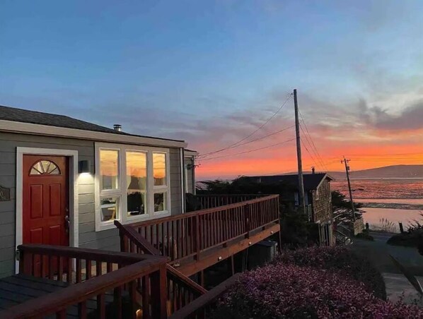 A house with a red door, a covered porch, and a view of the ocean at sunset.